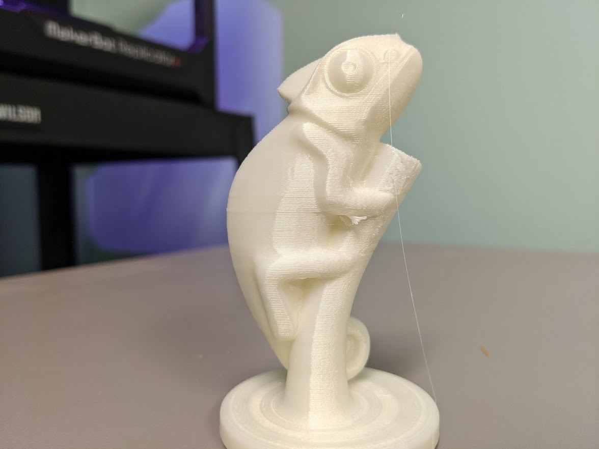 close up of the 3D printed chameleon pen holder showing a small triangle of filament under its arm and a thin thread of filament coming from its nostril